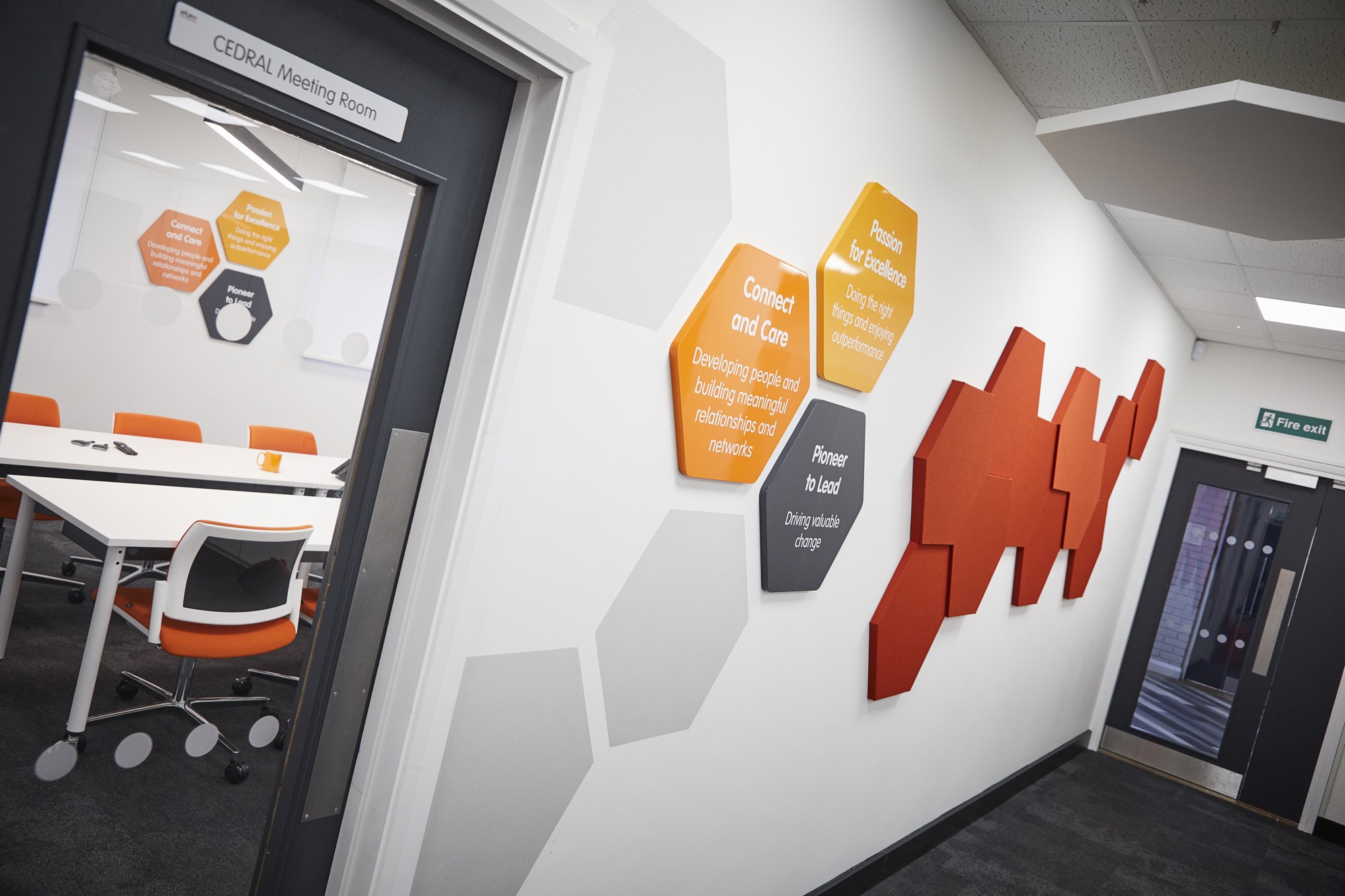 Hexagonal wall graphics in the corridor of Etex Facades. Through the window of a door, the image shows the same hexagonal design is repeated in a meeting room.